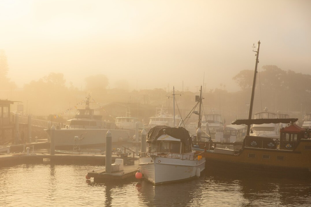 Foggy harbor at dawn with silhouettes of old boats